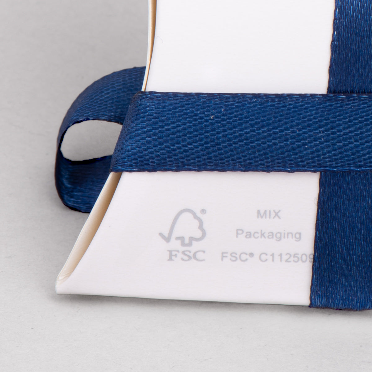 Dettaglio del packaging di Biloux. Nella foto si nota il marchio FSC sullo sfondo bianco della scatolina e il nastro blu notte che lo avvolge.