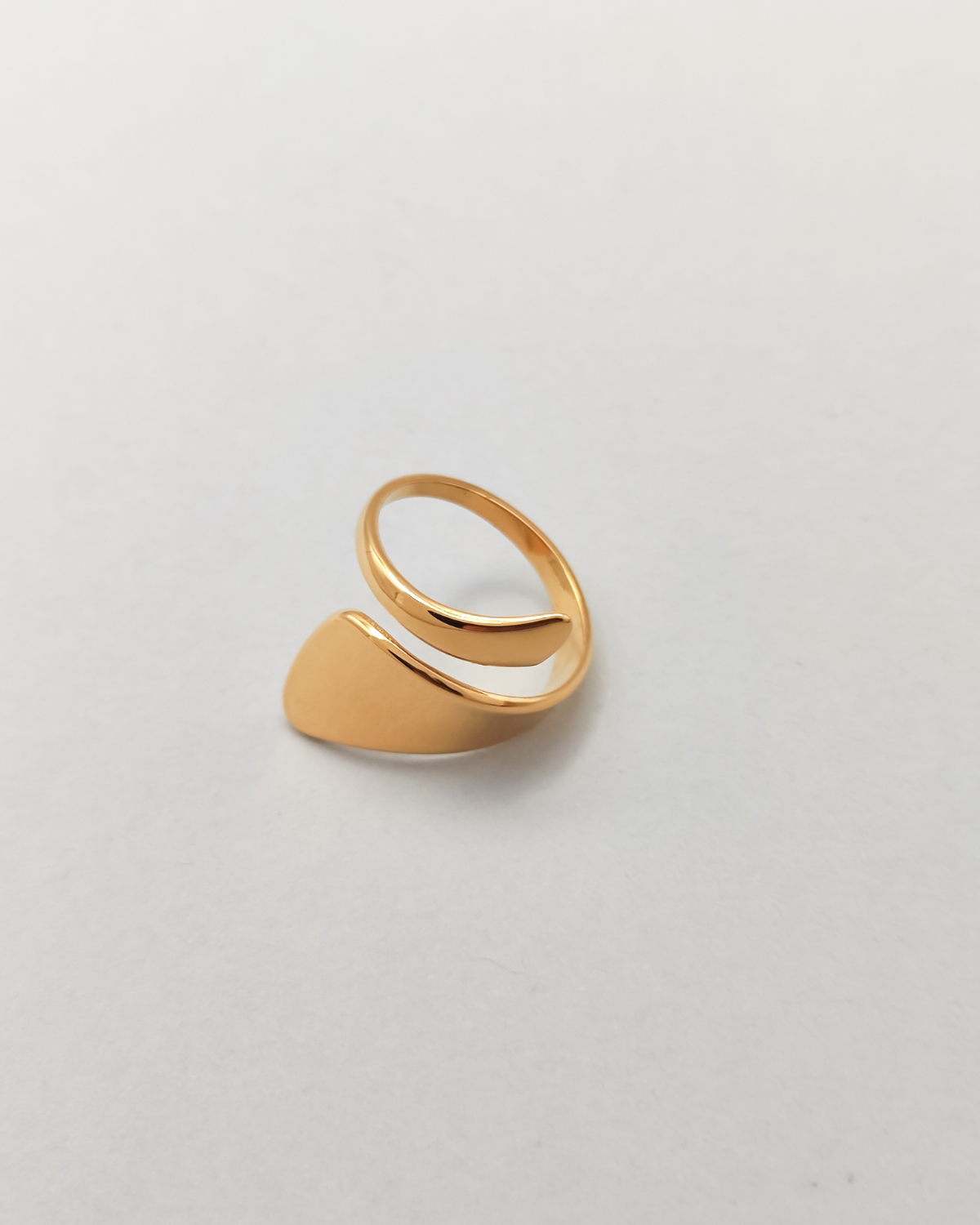 Anello Alice in acciaio inossidabile anallergico color oro. È rappresentato su sfondo grigio chiaro e si vede la forma a spirale più stretta da un lato e più larga dall'altro.