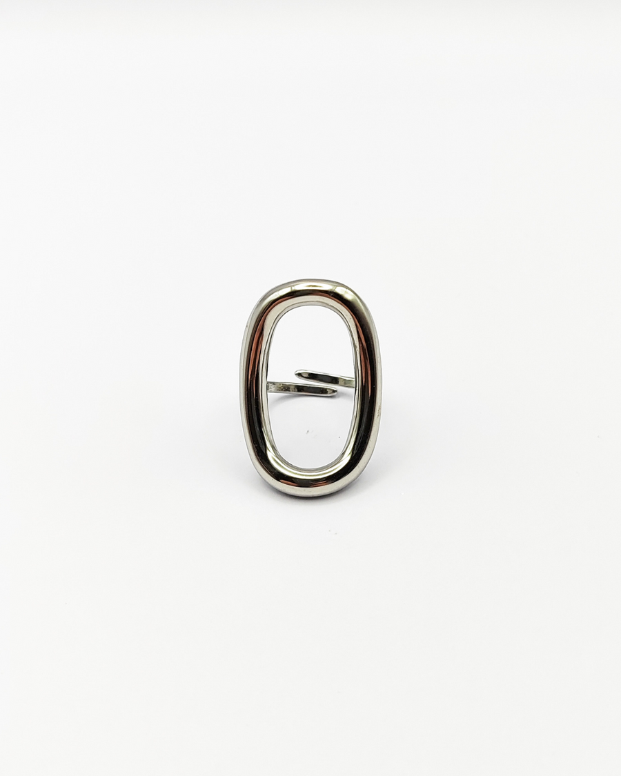 Anello Altea in acciaio inossidabile color argento. È fotografato frontalmente e attraverso l'ovale traforato che si trova sulla parte superiore, si può vedere la chiusura regolabile sul retro.