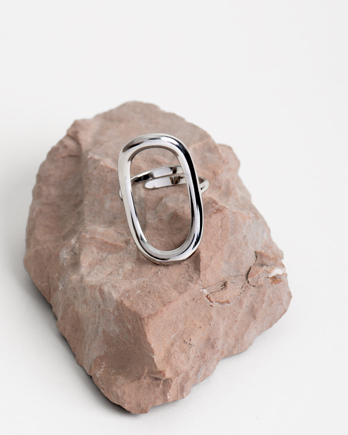 Anello Altea in acciao inossidabile color argento, rappresentato su una roccia rossastra e sfondo bianco. Si nota la lavorazione ovale traforata e la chiusura regolabile sul retro. 
