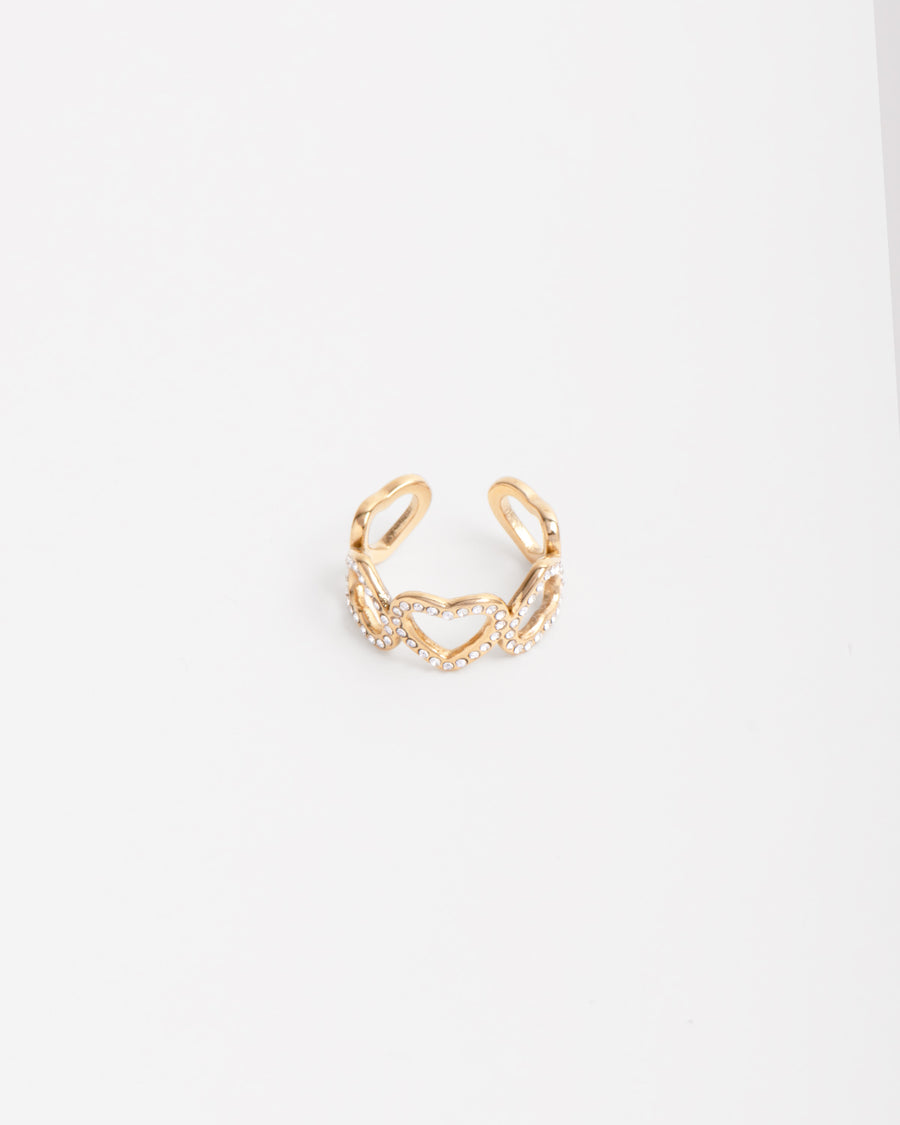 Anello Angelica in acciaio inossidabile color oro . Ha un design a fascia formato da 5 cuori: i tre centrali  hanno una fila di strass mentre i due finali sono lisci. Il verso dei cuori è alternato ed è regolabile sul retro.
