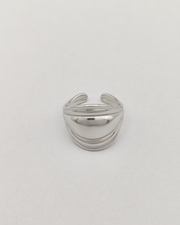 Anello Carlotta in acciaio inossidabile anallergico color argento. È rappresentato frontalmente su uno sfondo grigio chiaro. Ha una forma bombata al centro che si ristringe verso i lati ed ha un finish lucido e si vede la chiusura regolabile sul retro