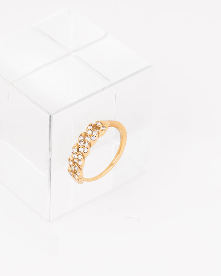 Anello Elisa affiancato ad un cubo di vetro. In acciaio inossidabile con strass, colorazione oro e regolazione a scomparsa. La lavorazione sulla parte superiore dell'anello è a treccia. È realizzato in materiale anallergico e resistente all'acqua.