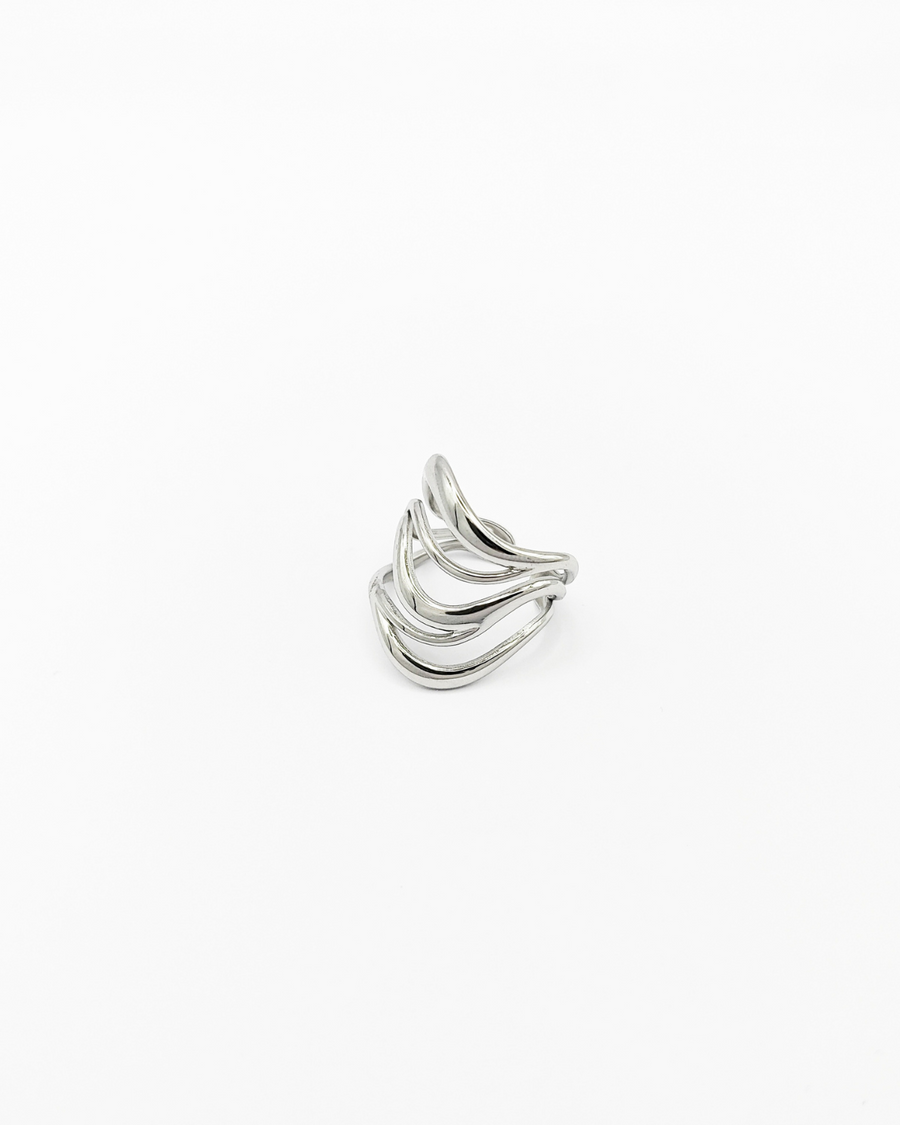 Anello Giulia in acciaio inossidabile color argento. È fotografato appoggiato su un lato in 3/4. Si vede il design a onde con il ricciolo sul lato inferiore, verso la chiusura.