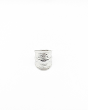 Anello Odine in acciaio inossidabile color argento. È fotografato frontalmente e lascia vedere bene la forma più larga al centro che si restringe verso il retro. Ha una fascia più sporgente al centro mentre verso le estremità il design è drappeggiato.