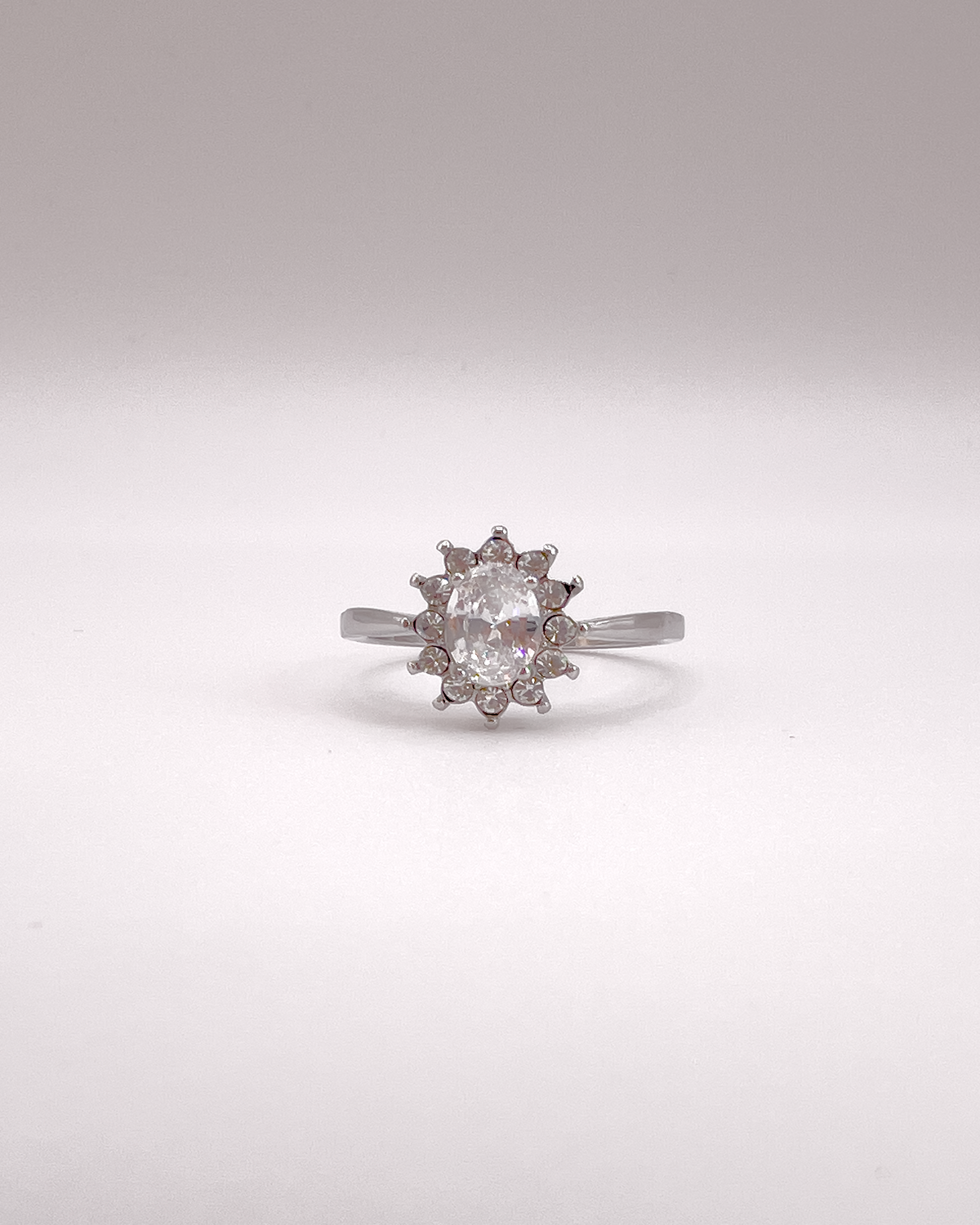 Anello Elisabetta, modello princess, in acciaio inossidabile color argento e zirconi. La pietra centrale è contornata da più pietre piccole. L'anello è ripreso frontalmente su uno sfondo grigio chiaro.