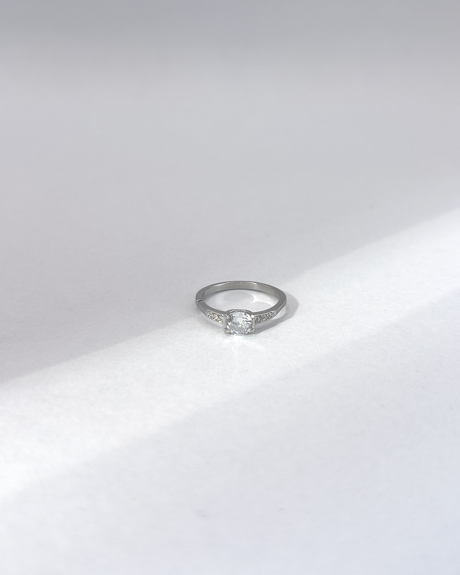 Anello Letizia in acciaio inossidabile anallergico in colore argento e zirconi. La pietra centrale è accompagnata da piccole pietre sui lati. E' rappresentato frontalmente su uno sfondo grigio.