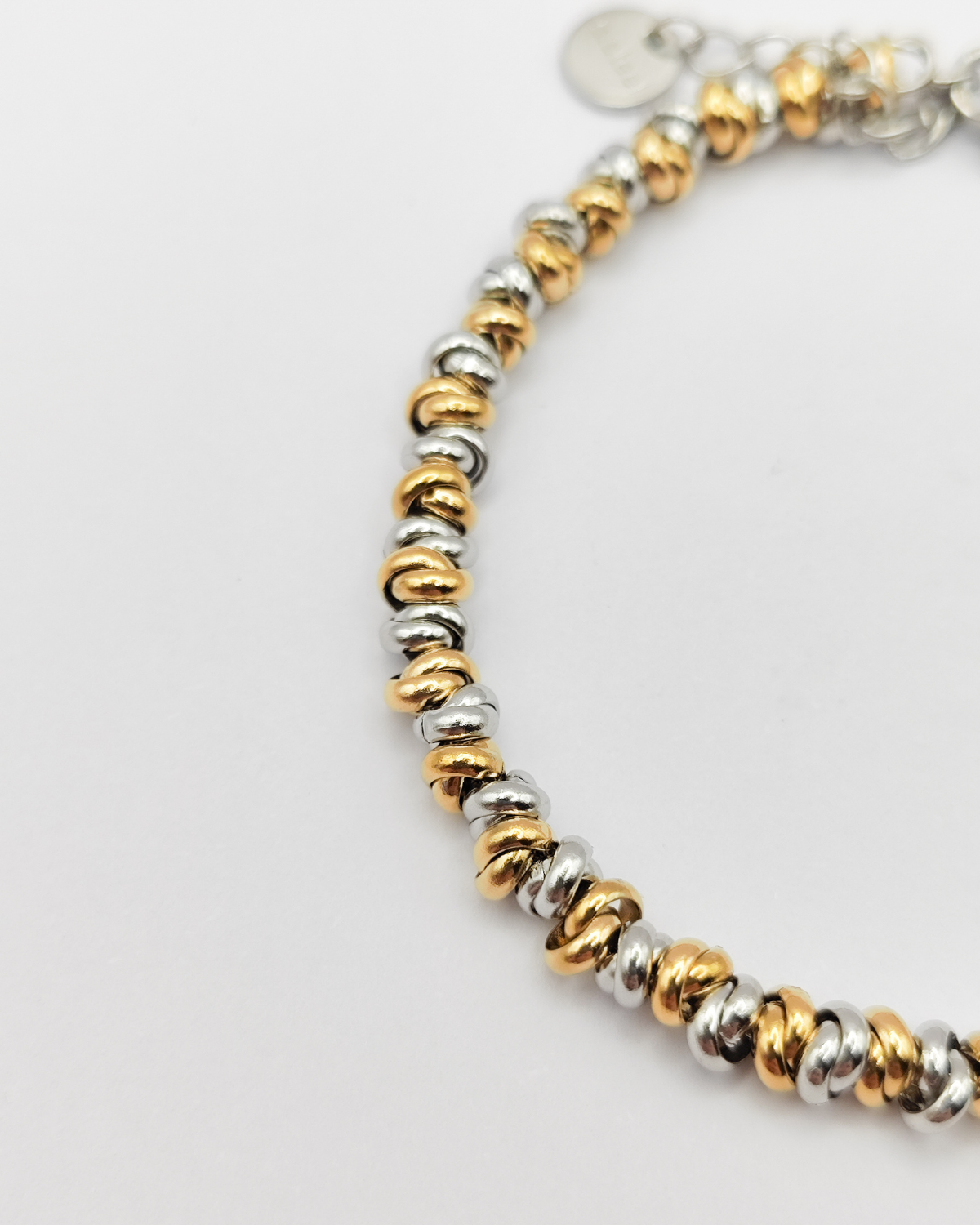 Dettaglio del bracciale Anna in acciaio inossidabile. È formato da una serie di nodini alternati di colore oro e argento, sullo sfondo si intravede la catenella che permette di regolare la lunghezza.
