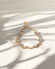 Bracciale Chiara in acciaio inossidabile e strass montati su castoni rotondi colore oro. È rappresentato chiuso ed adagiato a goccia su sfondo bianco sul quale si stagliano delle ombre allungate. I castoni alternano una misura grande ad una più piccola e sono distanziati da una catenella. La chiusura è a moschettone e si può regolare la lunghezza. Il materiale è waterproof e nichel free.