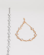 Coppia di bracciali Chiara in acciaio inossidabile e strass montati su castoni rotondi colore argento e oro su sfondo bianco. Il bracciale aragento è raffigurato aperto e disteso, mentre quello oro è chiuso e posizionato a goccia. I castoni alternano una misura grande ad una più piccola e sono distanziati da una catenella. La chiusura è a moschettone e si può regolare la lunghezza. Il materiale è waterproof e nichel free.