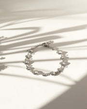Bracciale Chiara in acciaio inossidabile e strass montati su castoni rotondi colore argento. È rappresentato chiuso ed adagiato su sfondo bianco sul quale si stagliano delle ombre lunghe e sottili. I castoni alternano una misura grande ad una più piccola e sono distanziati da una catenella. La chiusura è a moschettone e si può regolare la lunghezza. Il materiale è waterproof e nichel free.