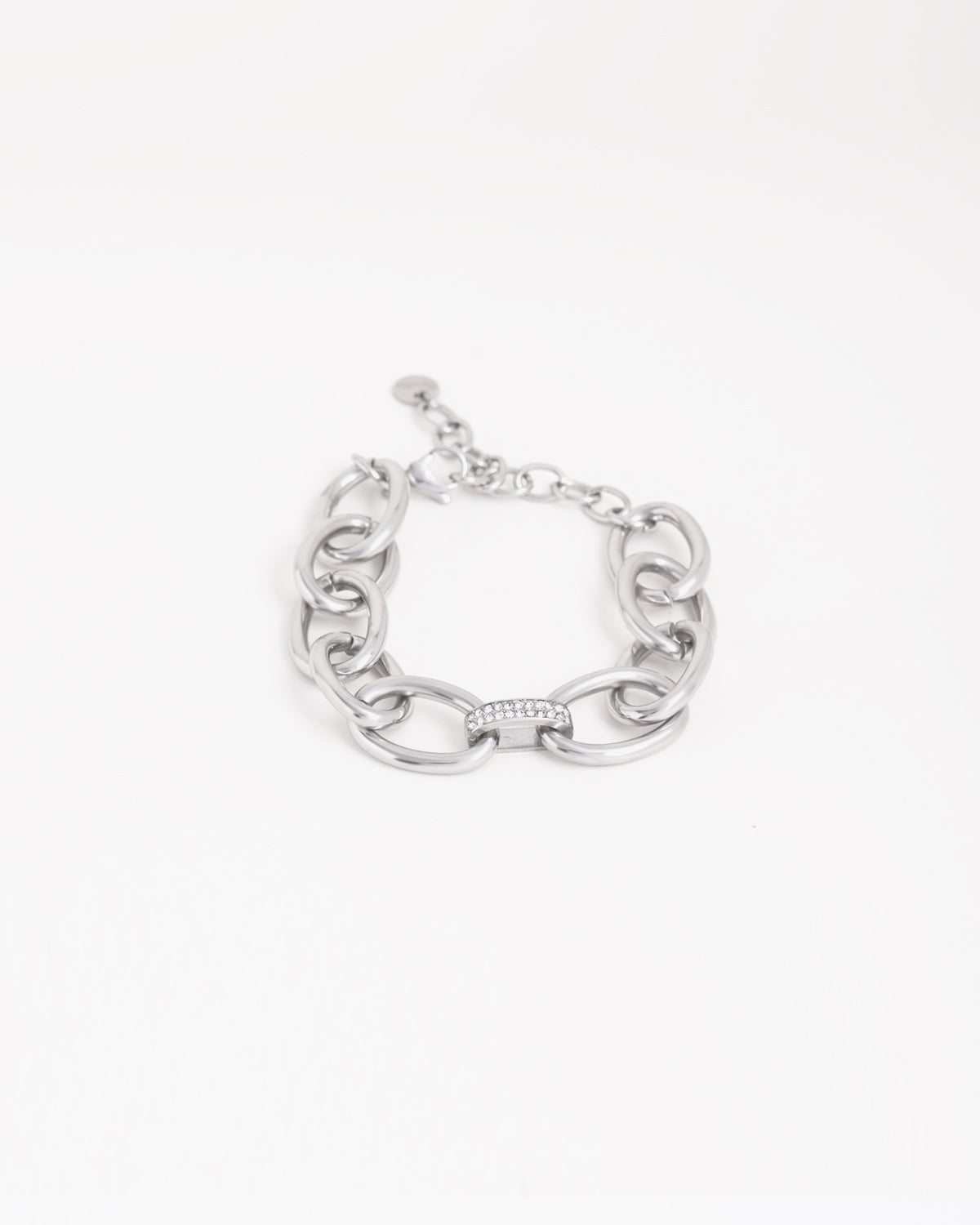 Bracciale Sandra in acciaio inossidabile a maglie larghe ovali color argento, con raccordo centrale a doppia fila di strass. È adagiato chiuso su uno sfondo chiaro. Come sempre è in materiale anallergico e waterproof. La chiusura è a moschettone con catenella per la regolazione.