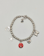 Bracciale Sara in acciaio inossidabile anallergico color argento con charms a forma di ferro di cavallo, stella, coccinella smaltata rossa, cuore e farfalla. Il bracciale è composto da perline martellate.