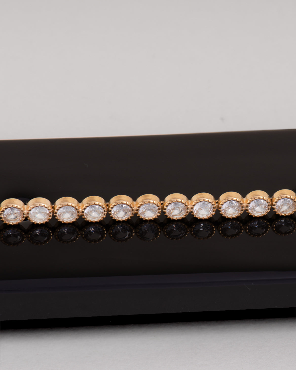 Bracciale Ylenia in acciaio inossidabile, anallergico e waterproof, modello tennis con strass montati su castoni rotondi zigrinati. È poggiato lateralmente su una superficie nera che lo riflette e il resto dello sfondo è bianco. 