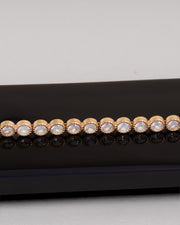 Bracciale Ylenia in acciaio inossidabile, anallergico e waterproof, modello tennis con strass montati su castoni rotondi zigrinati. È poggiato lateralmente su una superficie nera che lo riflette e il resto dello sfondo è bianco. 