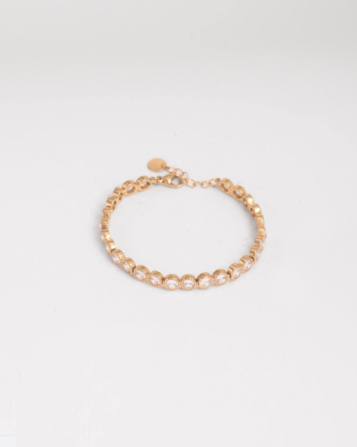 Bracciale Ylenia in acciaio inossidabile, anallergico e waterproof, modello tennis con strass montati su castoni rotondi zigrinati. È appoggiato chiuso su uno sfondo bianco ed è ben visibile sia la parte frontale del bracciale, sia il retro dei castoni. La chiusura è a moschettone e la lunghezza regolabile tramite una catenella.