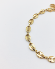 Dettaglio del bracciale Elena in acciaio inossidabile anallergico e waterproof color oro. E' composto da tanti ciondoli ovali legati a catena. E' regolabile e rappresentato su uno sfondo grigio chiaro.