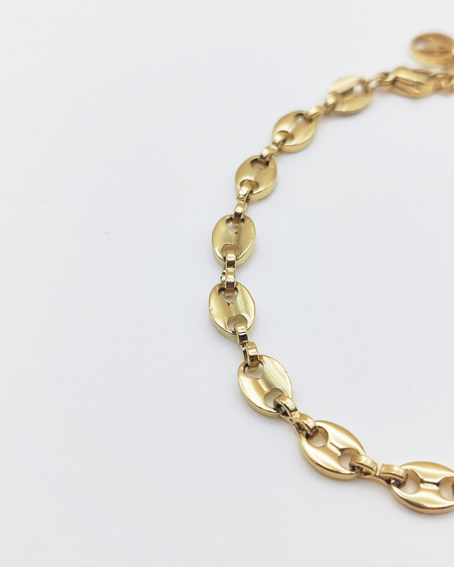 Dettaglio del bracciale Elena in acciaio inossidabile anallergico e waterproof color oro. E' composto da tanti ciondoli ovali legati a catena. E' regolabile e rappresentato su uno sfondo grigio chiaro.