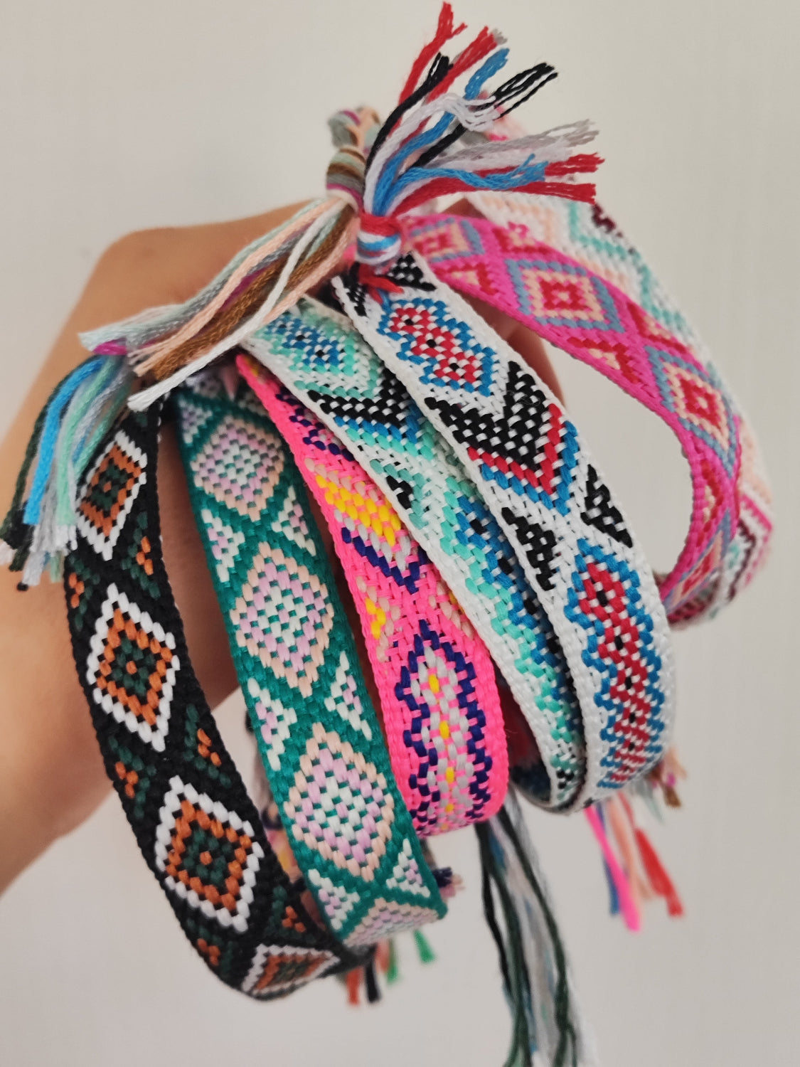 Bracciali in filo intrecciato di vari colori tenuti in mano insieme.