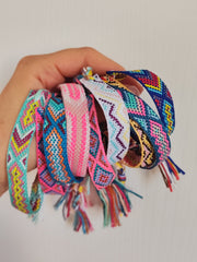 Bracciali in filo intrecciato di vari colori tenuti in mano insieme.
