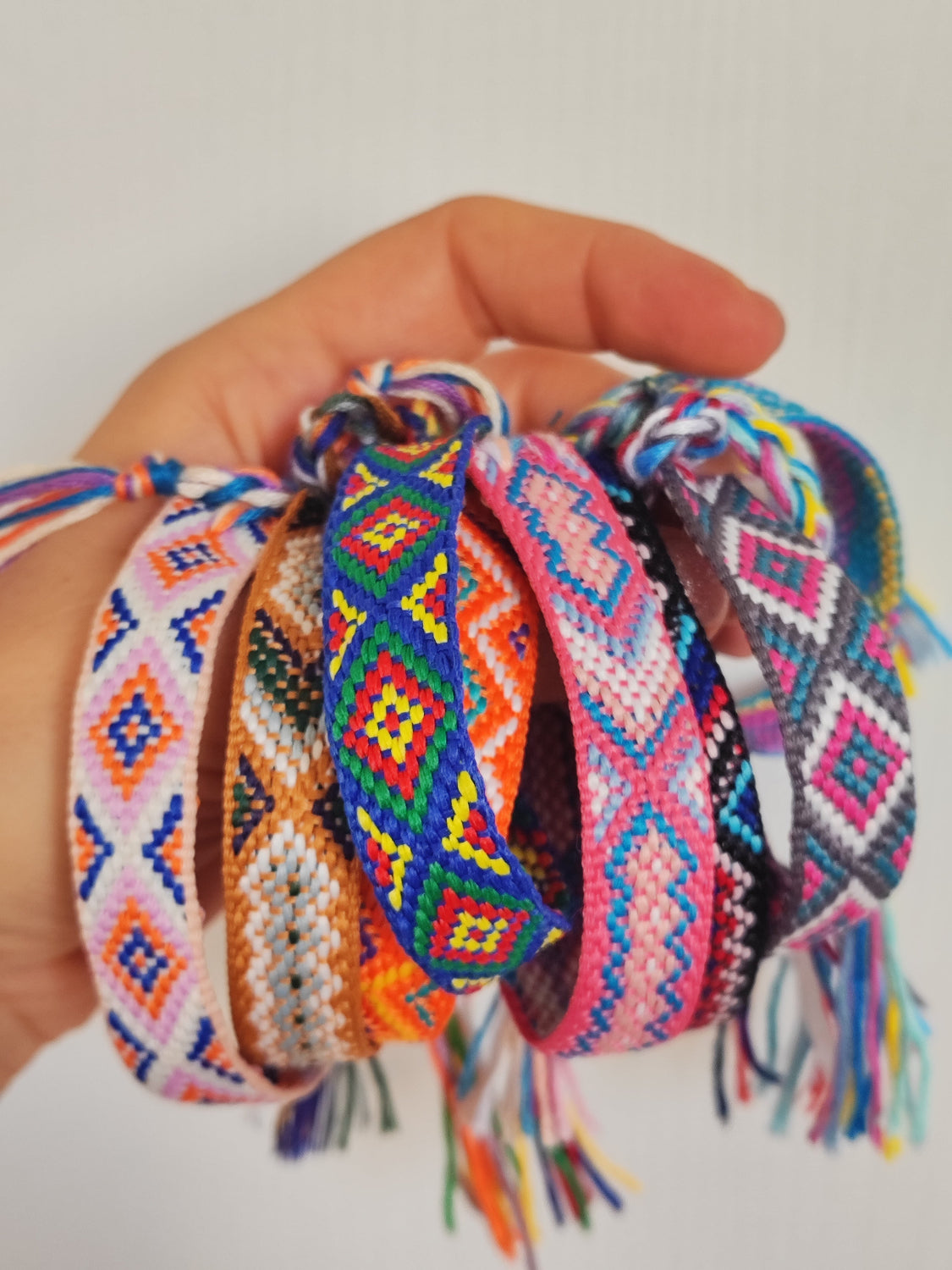 Bracciali in filo intrecciato di vari colori tenuti in mano insieme.