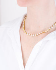 Collana Alessia in acciaio inossidabile color oro, modello tennis con strass indossata da una modella con camicia bianca. I castoni hanno una forma rotonda e sono uniti da una singola maglia. E'un modello a girocollo che però si può allungare.