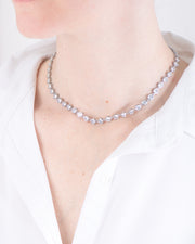 Collana Alessia in acciaio inossidabile color argento, modello tennis con strass indossata da una modella con camicia bianca. I castoni hanno una forma rotonda e sono uniti da una singola maglia. E'un modello a girocollo che però si può allungare.