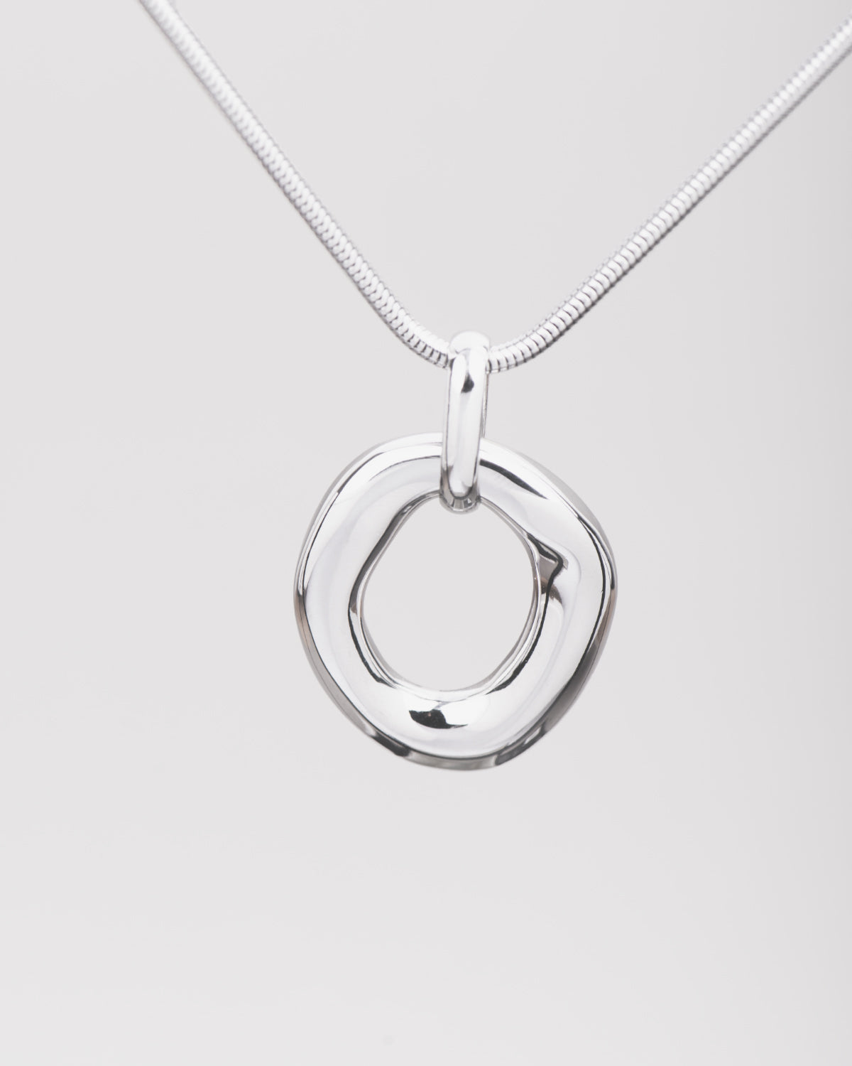 Collana Denise in acciaio inossidabile color argento. Il focus è sul ciondolo ovale di forma irregolare e traforato. Si vede anche la catena in stile coda di topo.