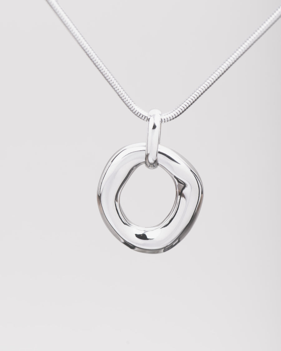 Collana Denise in acciaio inossidabile color argento. Il focus è sul ciondolo ovale di forma irregolare e traforato. Si vede anche la catena in stile coda di topo.