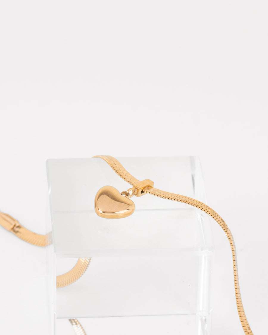 Collana Emma con catena piatta e pendaglio a forma di cuore dal finish lucido. Il dettaglio del ciondolo è rappresentato appoggiato ad un cubo di vetro che lo mette in risalto. È un gioiello in acciaio inossidabile, anallergico e resistente all'acqua.