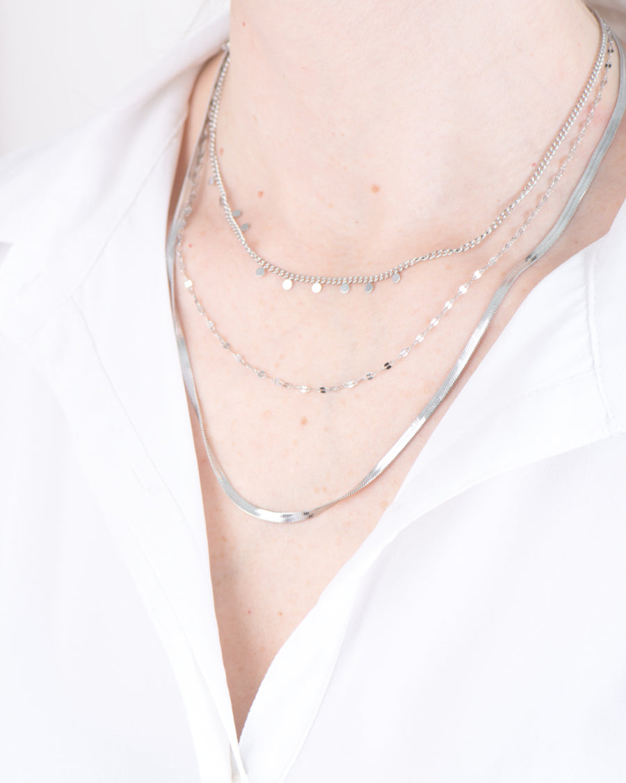 Collana Moira in acciaio inossidabile color argento. È composta da tre fili diversi: il primo, più corto, è una catenella con delle medagliette tone, il secondo è una canetenella liscia mentre il terzo, il più lungo, è un modello snake.