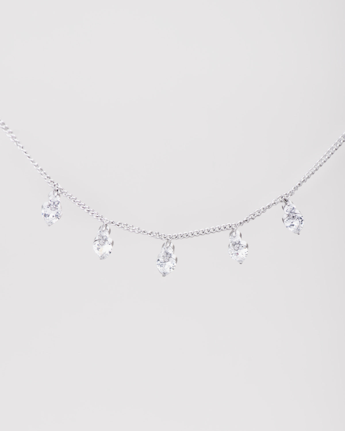 Collana Stefania in acciaio inossidabile color argento e pendenti a forma di cuore in strass. Dalla catenina pendono 5 cuoricini luminosi, sormontati a loro volta da un piccolo brillantino.