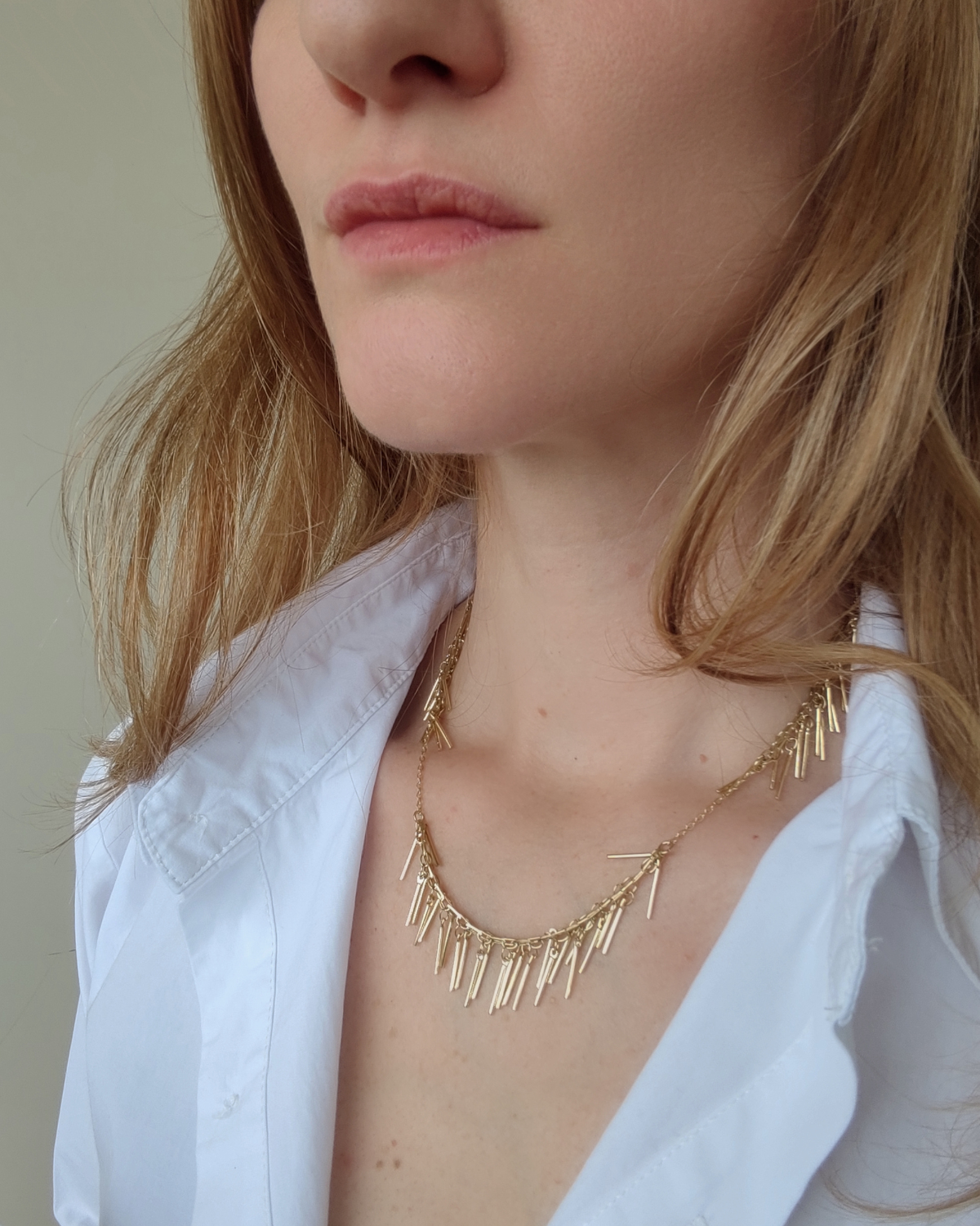 Collana Francesca in acciaio inossidabile color oro con nappine in acciaio indossata da una modella con capelli biondi e camicia bianca.