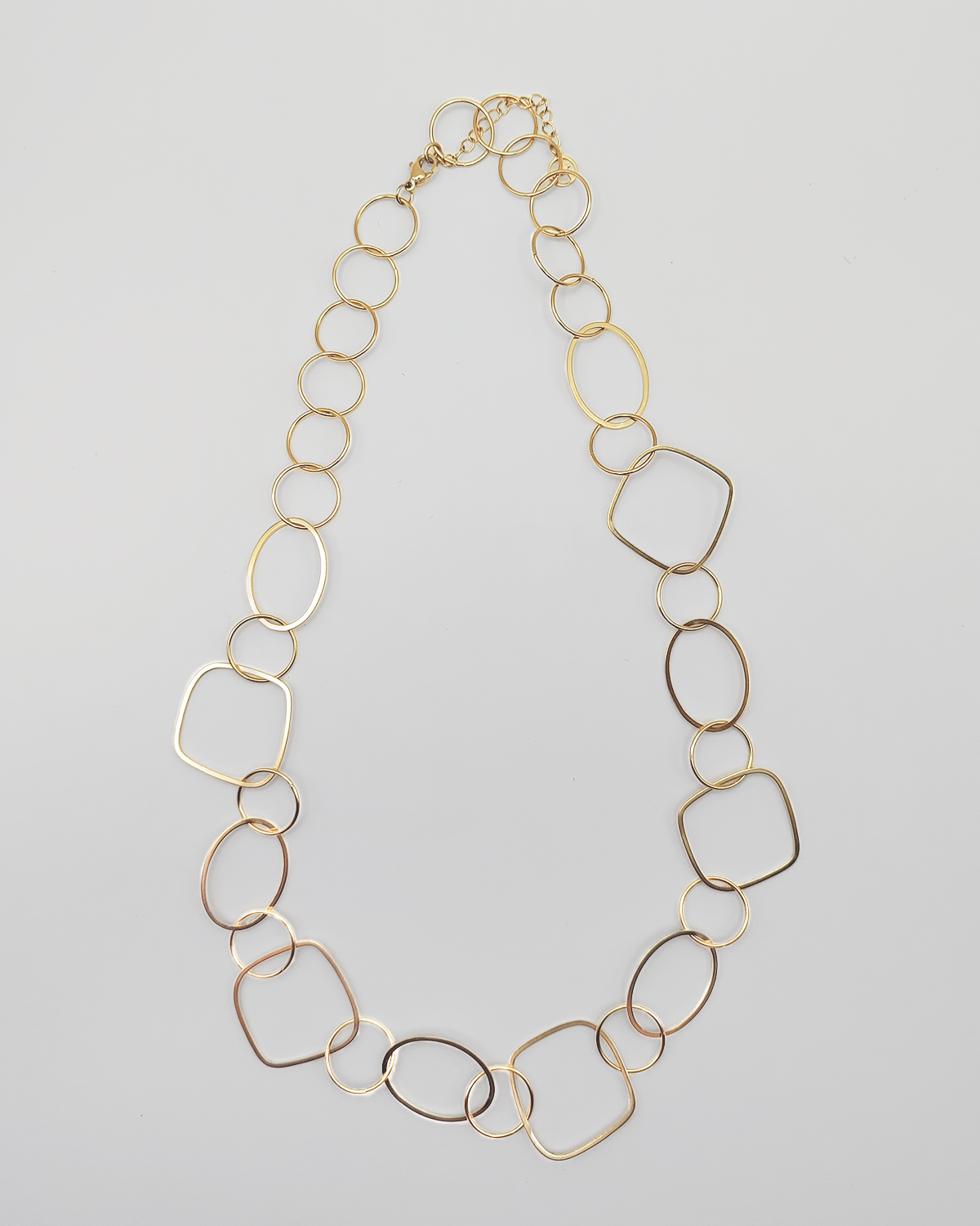 Collana Liliana in acciaio inossidabile e anallergico, formata da tanti ciondoli di diverse forme geometriche. Molto fine ed elegante, è ripresa dall'alto su uno sfondo grigio chiaro.