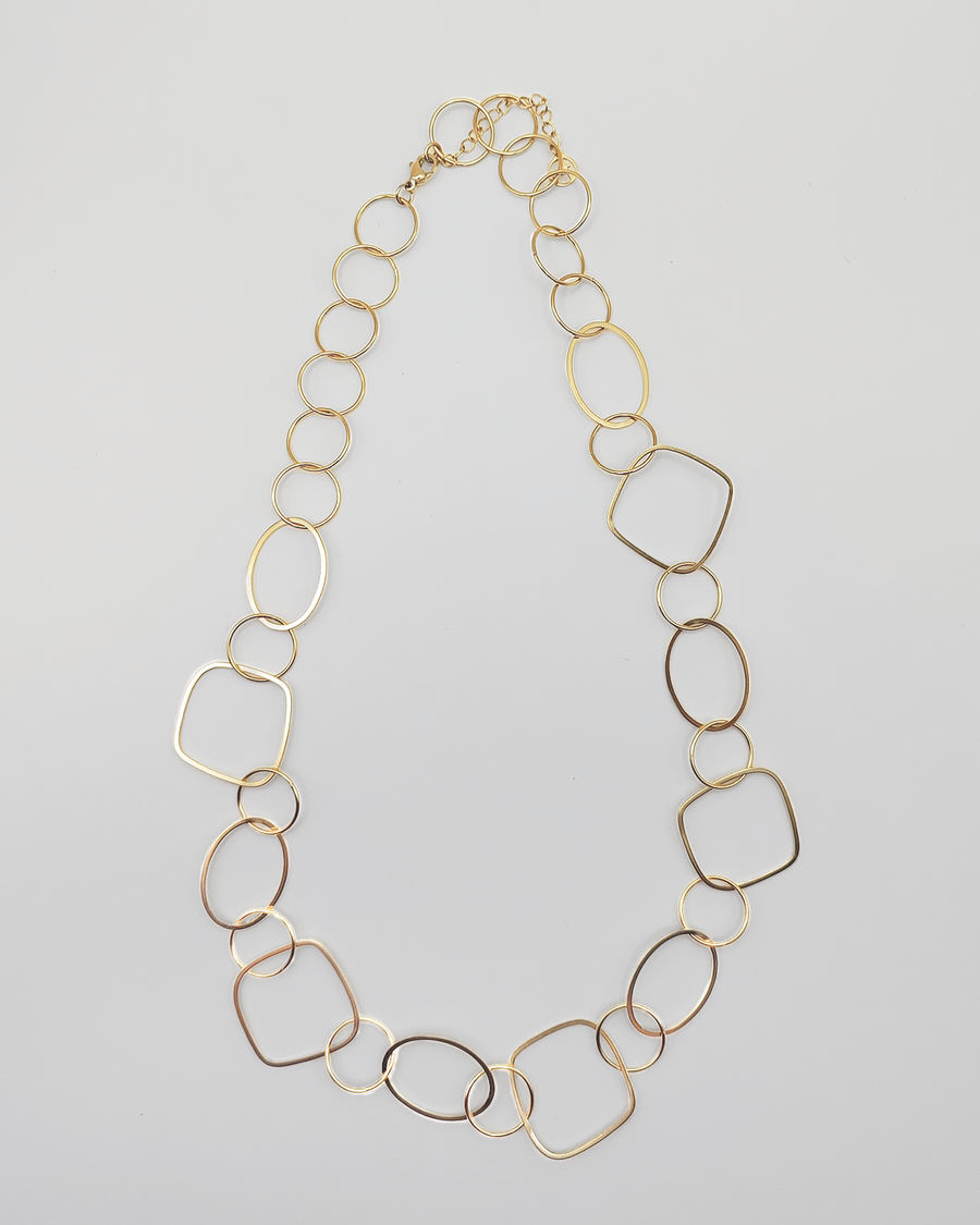 Collana Liliana in acciaio inossidabile e anallergico, formata da tanti ciondoli di diverse forme geometriche. Molto fine ed elegante, è ripresa dall'alto su uno sfondo grigio chiaro.