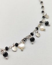 Dettaglio della collana Marta in acciaio inossidabile anallergico color argento. È decorata con charms a forma di cuoricino, cristalli neri e perle di fiume.