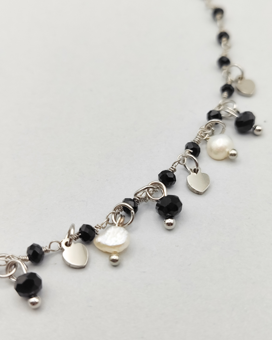 Dettaglio della collana Marta in acciaio inossidabile anallergico color argento. È decorata con charms a forma di cuoricino, cristalli neri e perle di fiume.