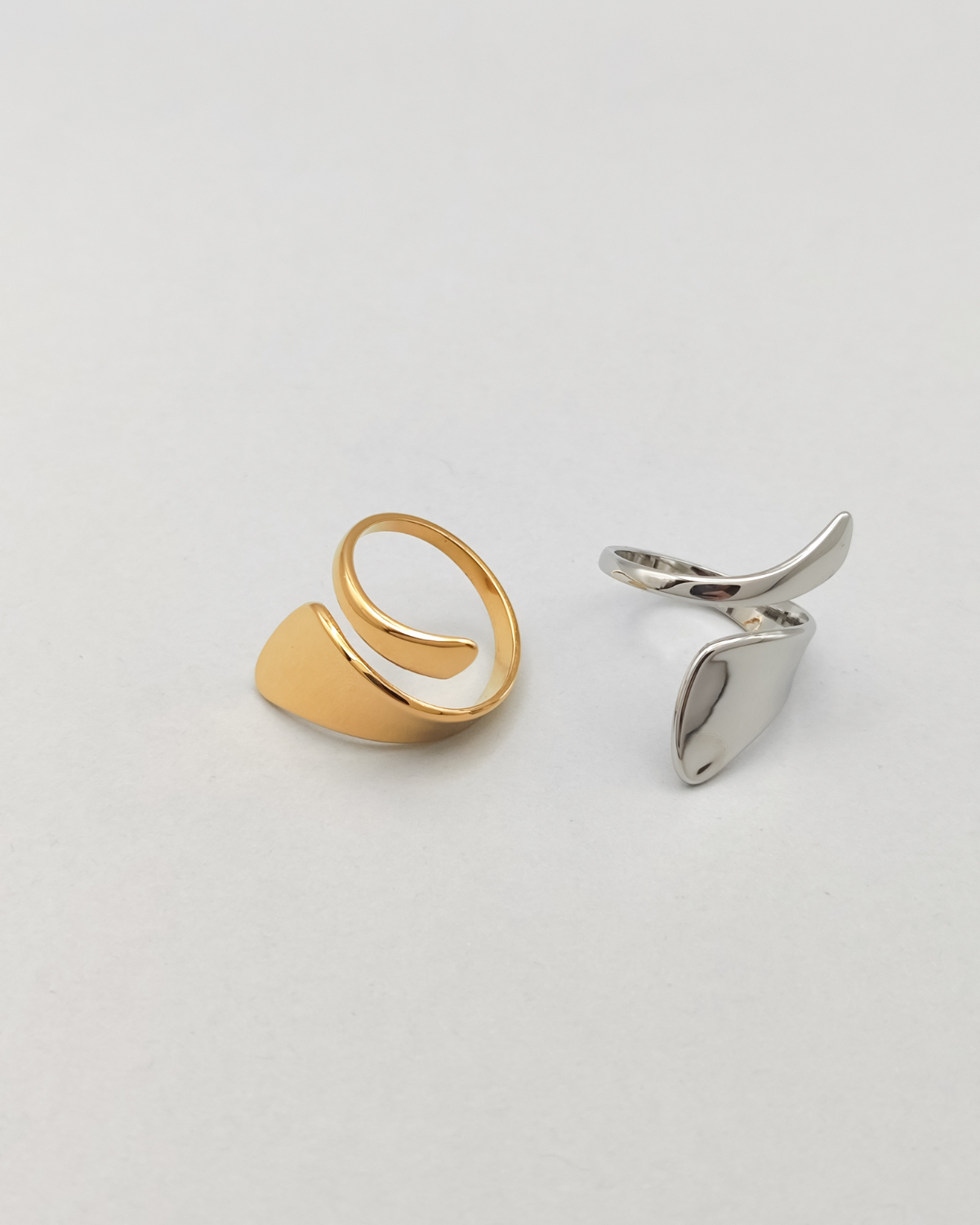 Coppia di anelli Alice in acciaio inossidabile anallergico color oro e argento su sfondo grigio chiaro e si vede la forma a spirale più stretta da un lato e più larga dall'altro. L'anello di sinistra è dorato mentre quello di destra è argentato