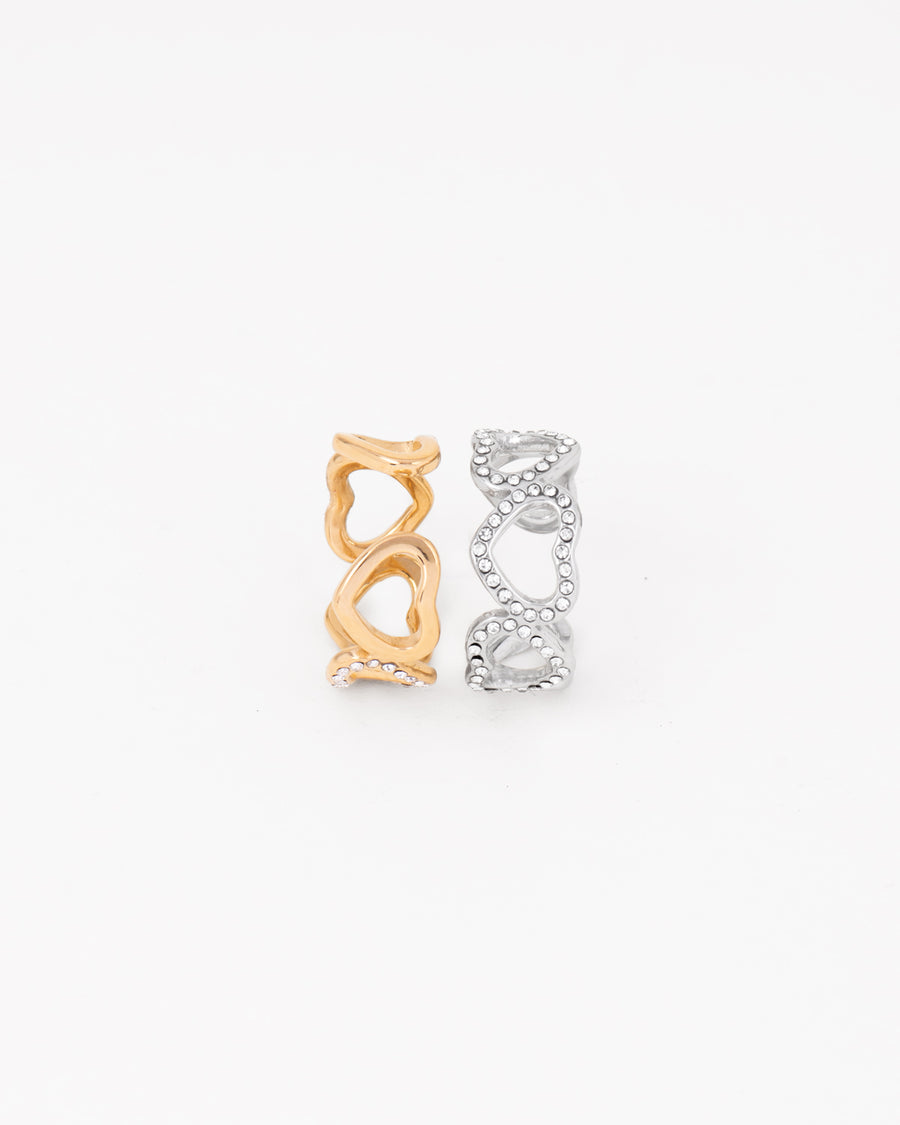Coppia di anelli Angelica in acciaio inossidabile e strass rappresentati in piedi e affiancati su sfondo bianco nelle colorazioni oro e argento. Il modello è una fede traforata formata da cuori traforati e coperti di strass nella parte frontale. Il retro è regolabile e in acciaio liscio lucido. Sono entrambi resistenti all'acqua e anallergici.