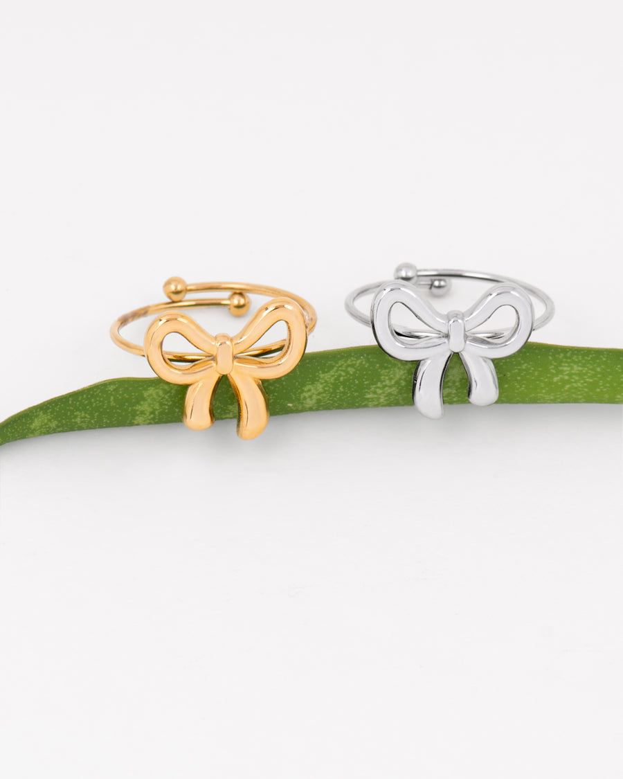 Coppia di Anelli Pamela, regolabili in acciaio inossidabile decorati da un fiocco anch'esso in acciaio, colorazione argento e oro. Sono appoggiati su una foglia verde che li sorregge. L'acciaio è un materiale anallergico e waterproof. È un anello raffinato e delicato.