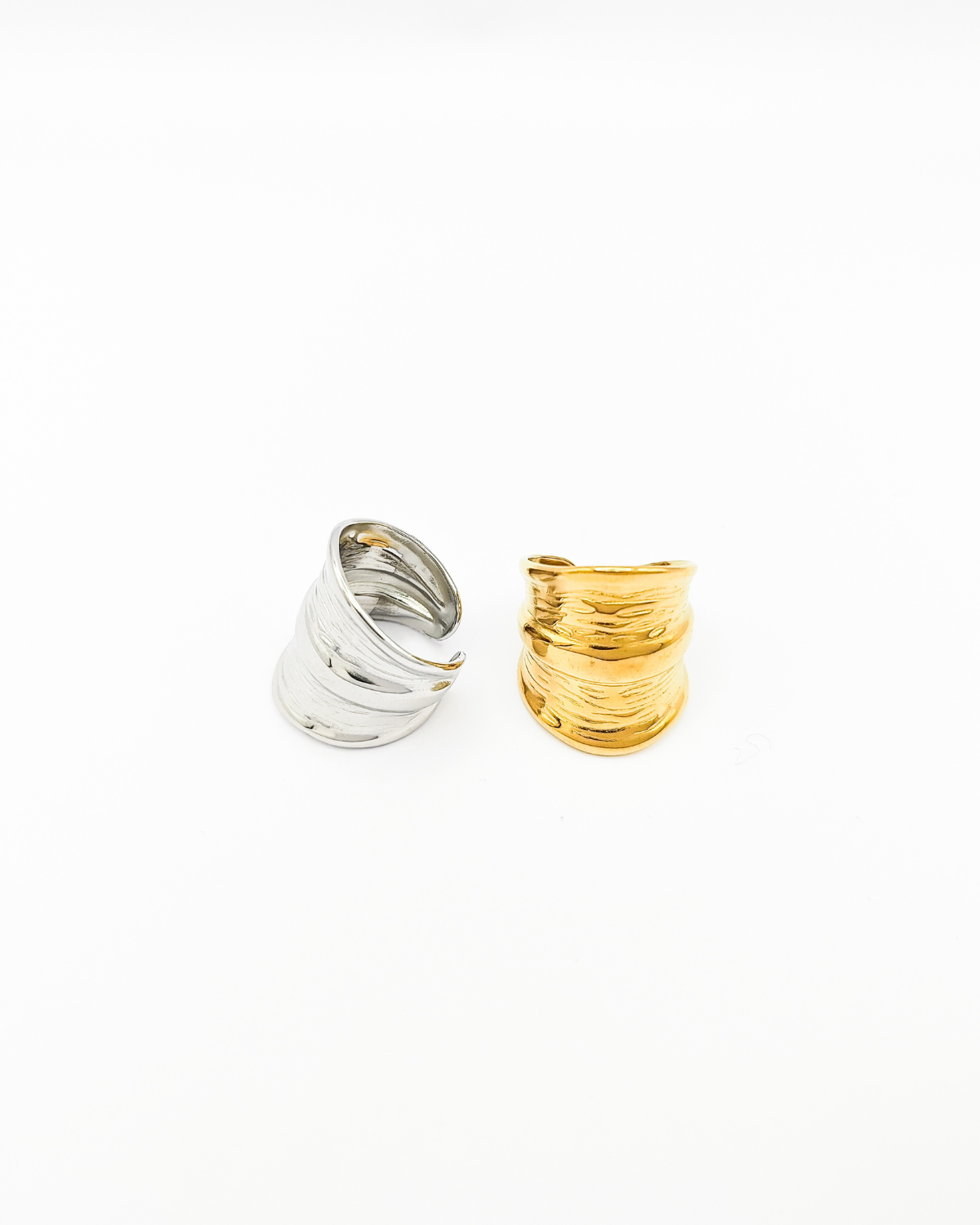 Coppia di anelli Odine in acciaio inossidabile colo argento e oro. L'anello argento è rappresentato in 3/4 e fa vedere il retro regolabile, quello oro è fotografato frontalmente e evidenzia il design a onde con una fascia più spessa al centro.