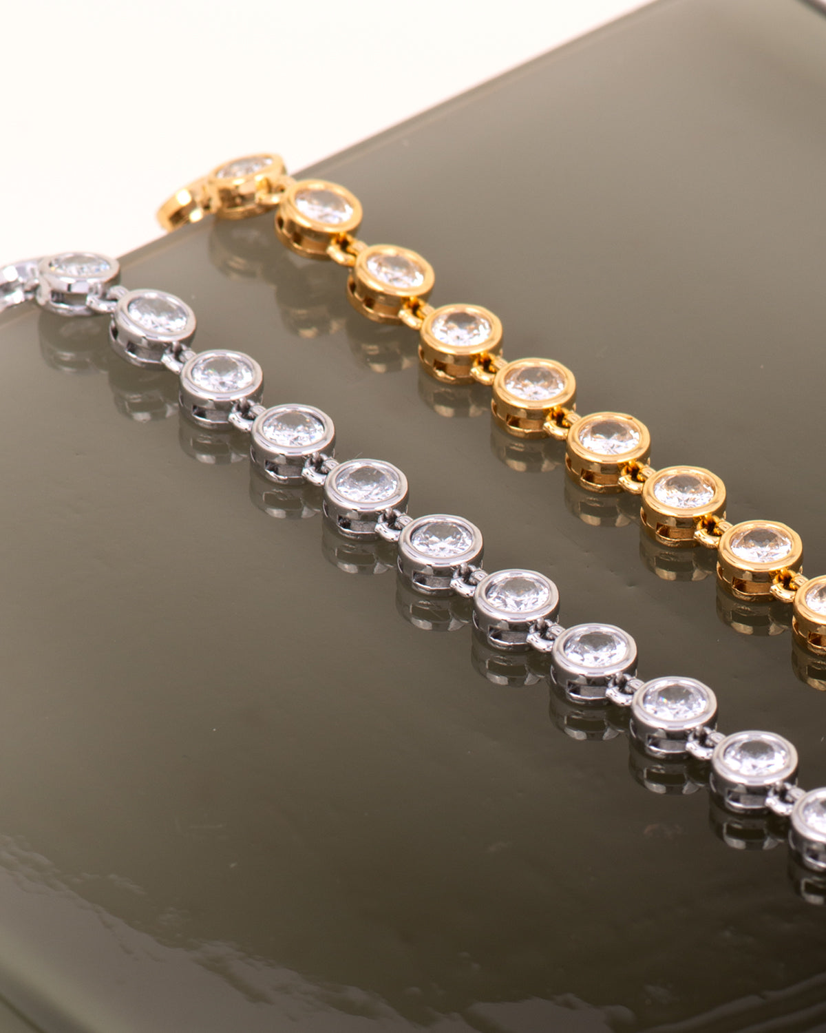 Coppia di bracciali Alessia, modello tennis con strass e castoni rotondi e piatti, senza griffe. Sono sia eleganti che sportivi e nella foto risaltano in quanto poggiati su uno sfondo nero lucido. Anche loro sono in materiale anallergico e resistente all'acqua.