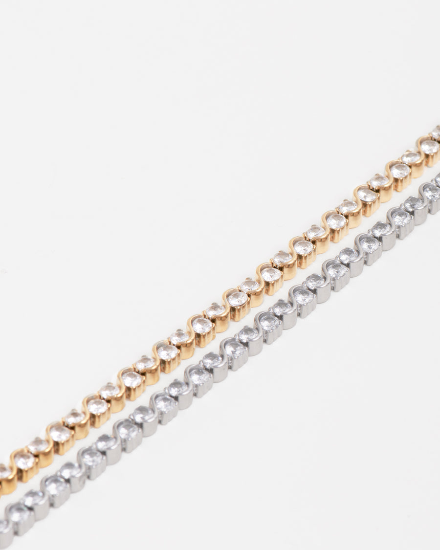 Coppia di bracciali Monica, in acciaio inossidabile e strass, modello tennis con motivo ad S. Sono rappresentati su sfondo bianco: il bracciale di destra è di color oro mentre quello di sinistra è argento.