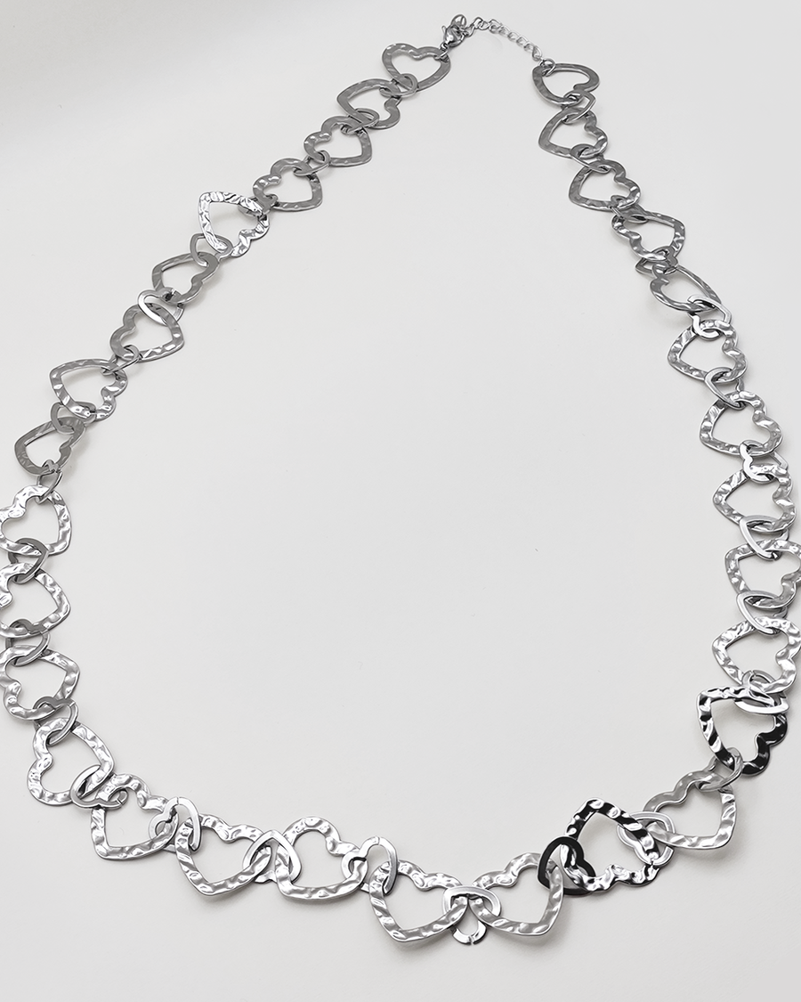 Collana Teresa in color silver. E' formata da tanti cuori in acciaio martellato intrecciati tra loro. E' ripresa su uno sfondo grigio chiaro.