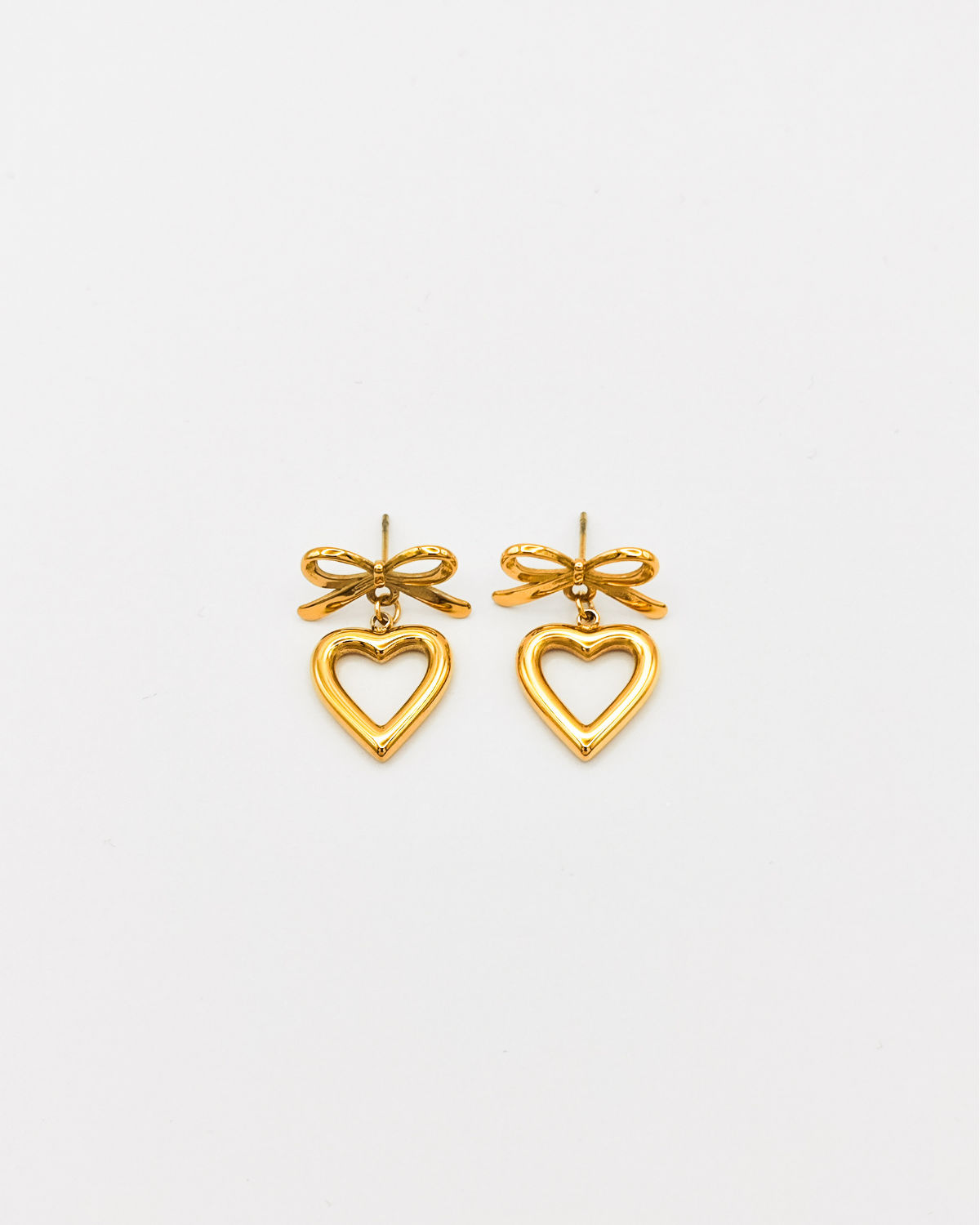 Orecchini Emma in acciaio inossidabile color oro. Sono formati da un fiocchetto che si fissa al lobo con una chiusura a perno, e un pendente a forma di cuore traforato.