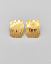 Gli orecchini Marika in acciaio inossidabile anallergico color oro sono rappresentati frontalmente su uno sfondo grigio chiaro. Hanno una forma rettangolare con delle righe verticali leggermente ondulate.