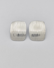 Gli orecchini Marika in acciaio inossidabile anallergico color argento sono rappresentati frontalmente su uno sfondo grigio chiaro. Hanno una forma rettangolare con delle righe verticali leggermente ondulate.