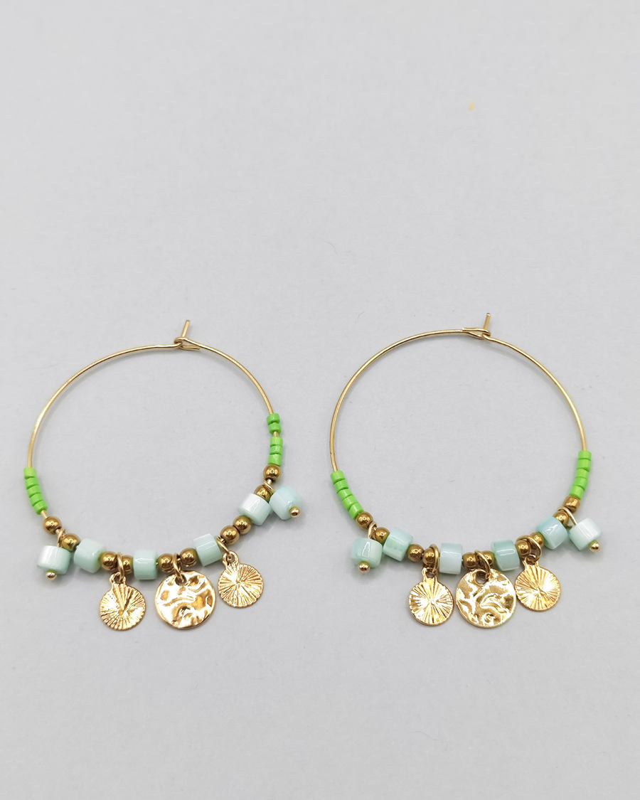 Orecchini Mascia in acciaio inossidabile anallergico color oro. Hanno una forma a cerchio e sono arricchiti da perline e pietre colore verde e charms dorati.