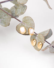 Doppia coppia di orecchini Matilde in acciaio inossidabile color oro in due versioni: lucidi o con centro in madreperla, entrambi in forma ovale. Sono appesi a delle foglie di eucalipto su uno sfondo bianco.