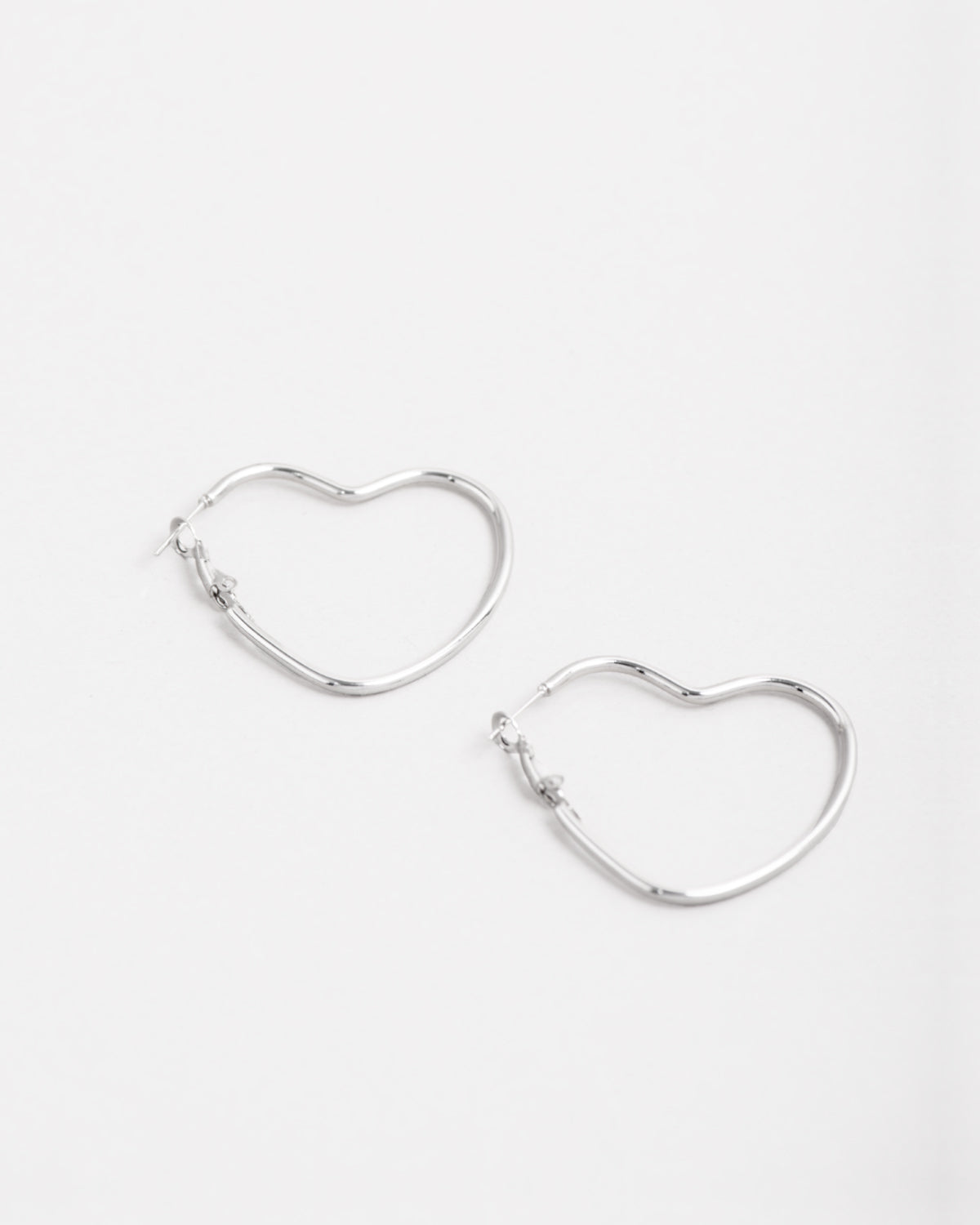 Orecchini Silvia in acciaio inossidabile color argento. Sono un modello a cerchio a forma di cuore ed hanno la chiusura a monachella. Sono rappresentati affiancati e l'orecchino di sinistra è leggermente più in alto di quello a destra.